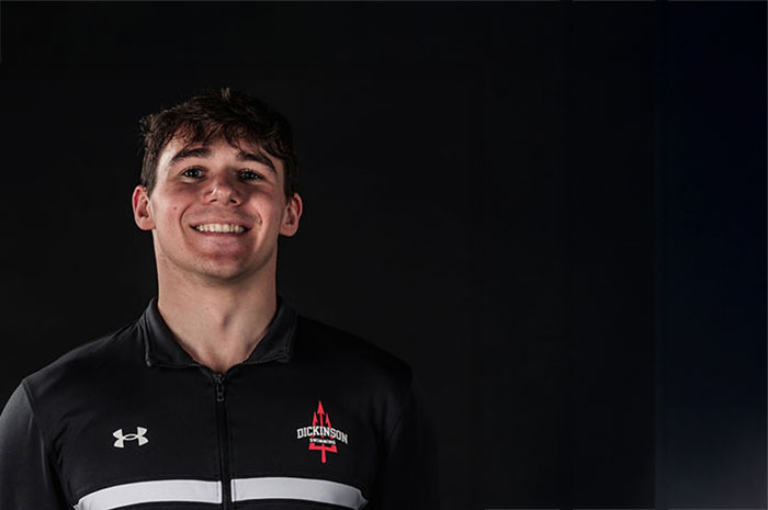 A young man in a black swim uniform against a black background.