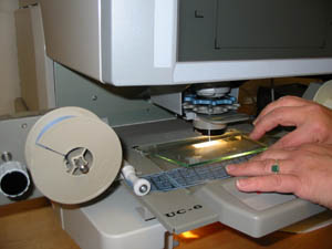 hands feeding microfilm beneath reader glass