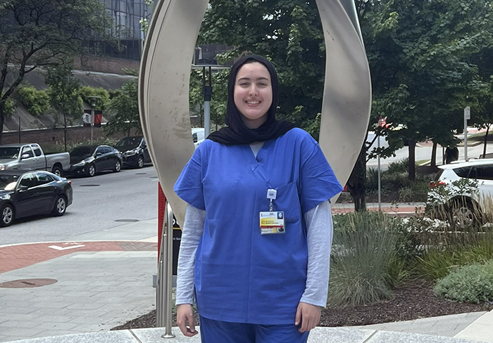 a young woman in scrubs poses in front of a medical center.