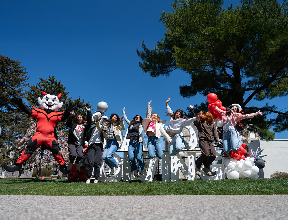 Students jump for a photo with the Dickinson Red Devil mascot during Day of Giving 2026