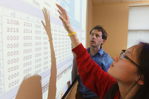 A student and professor look at a projection of computer code on a whiteboard.