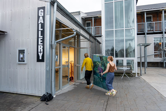 Two studio-art majors in the class of 2023 bring a painting into the Goodyear Gallery for a joint works-in-progress show. The final exhibition will open in the spring. Photo by Dan Loh.